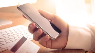 Person's hand holding a credit card and smartphone.