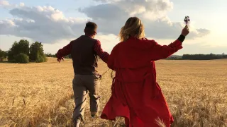 Couple running through a wheat field towards the setting sun.