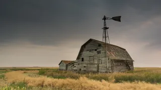 Old weathered barn with windmill in a field.