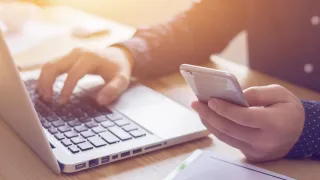 Man working on laptop while holding mobile phone