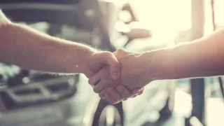 two people shaking hands in the foreground with car in background