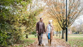 Couple walking their dog on a path in a park.