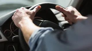 Hands holding a car steering wheel.
