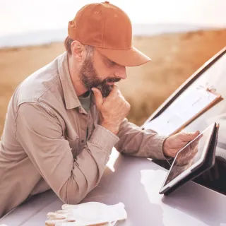 Farmer leaning on the hood of a truck using a tablet, golden hour