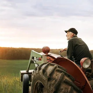 Farmer on a red tractor in a field at sunset.