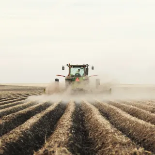 Tractor plowing a field, kicking up dust.