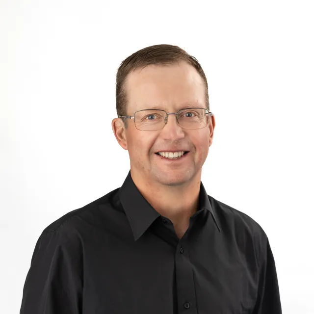 Man with glasses smiling, wearing a black button-up shirt.