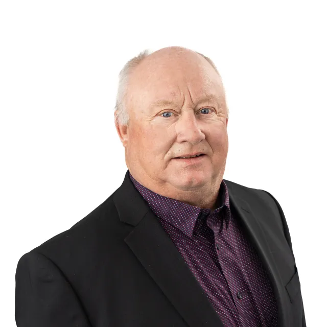 Older man in black suit and purple shirt, smiling.