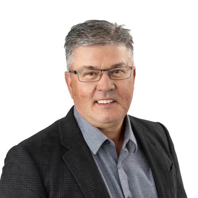 Headshot of a smiling middle-aged man wearing glasses and a blazer.