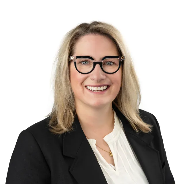 Smiling woman with blonde hair, wearing glasses and a black blazer.